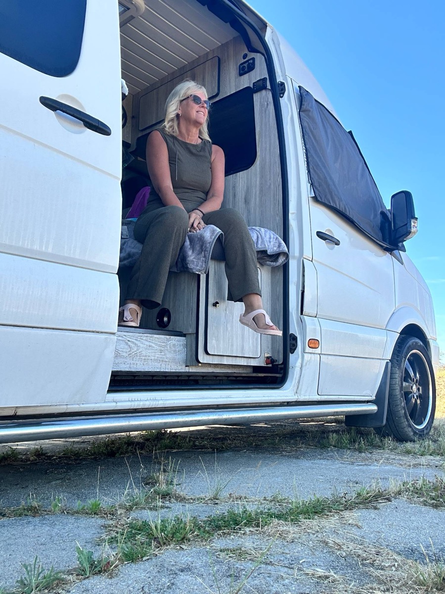 Yvonne sitting in the open side door of her campervan in the sunshine